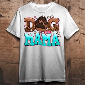 May include: White t-shirt featuring a graphic design of a paw print, bones, and the text "Dog Mama" in pink, brown, and blue.