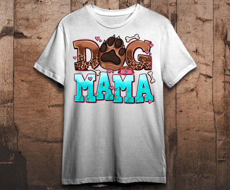 May include: White t-shirt featuring a graphic design of a paw print, bones, and the text "Dog Mama" in pink, brown, and blue.