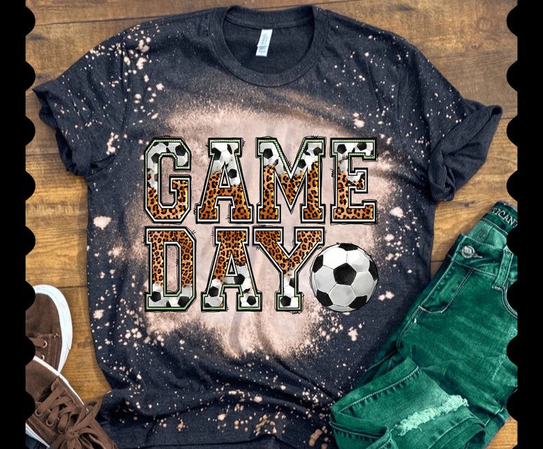 Pu&ograve; includere: Maglietta nera con effetto sbiancato e le parole "GAME DAY" in lettere bianche con un design a stampa leopardata. Un pallone da calcio &egrave; presente nel design.