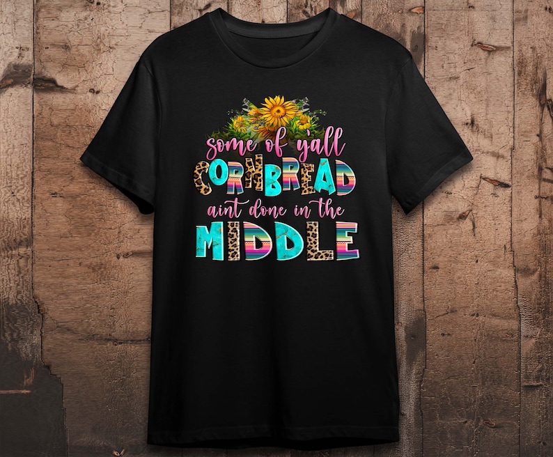 Pode incluir: Camiseta preta com um design gr&aacute;fico que apresenta girass&oacute;is e o texto "some of yall cornbread ain't done in the middle".
