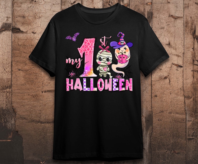 K&ouml;nnte beinhalten: Schwarzes T-Shirt mit einer pinkfarbenen und wei&szlig;en Grafik einer Mumie und eines Geistes. Die Grafik lautet "my 1st Halloween".