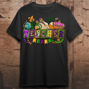 May include: Black t-shirt with a Mardi Gras themed design featuring the word "TEACHER" in colorful blocks with beads, flags, and a crown.