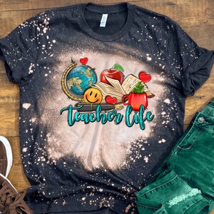 May include: Black t-shirt with a bleach-splattered design featuring a globe, book, apple, pen, and coffee mug. The text "Teacher Life" is written in blue and green lettering.
