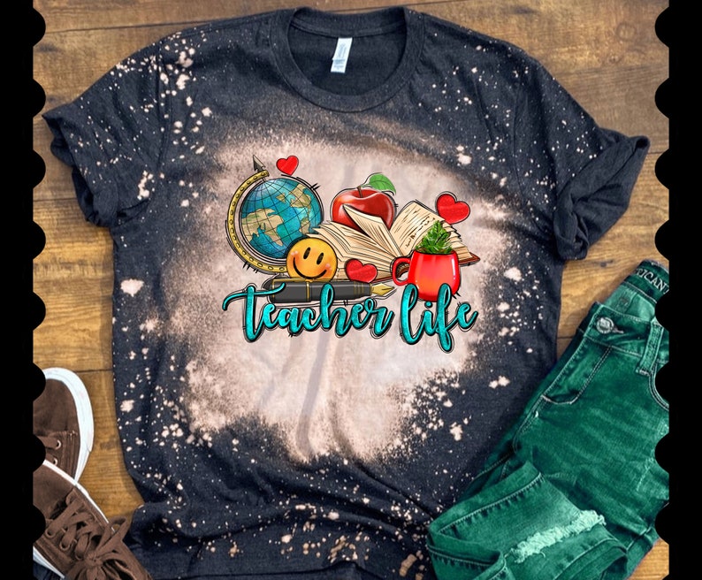 May include: Black t-shirt with a bleach-splattered design featuring a globe, book, apple, pen, and coffee mug. The text "Teacher Life" is written in blue and green lettering.