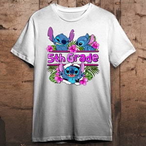 Op de afbeelding: Wit T-shirt met een blauw Stitch-personage ontwerp. Het Stitch-personage draagt een lei en er zijn roze bloemen en palmbladeren omheen. De tekst "5th Grade" is in roze letters op het shirt gedrukt.
