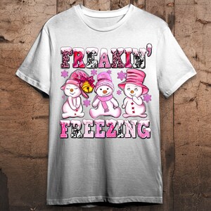 May include: White t-shirt with a pink and white graphic of three snowmen with the text "Freakin' Freezing" on it.
