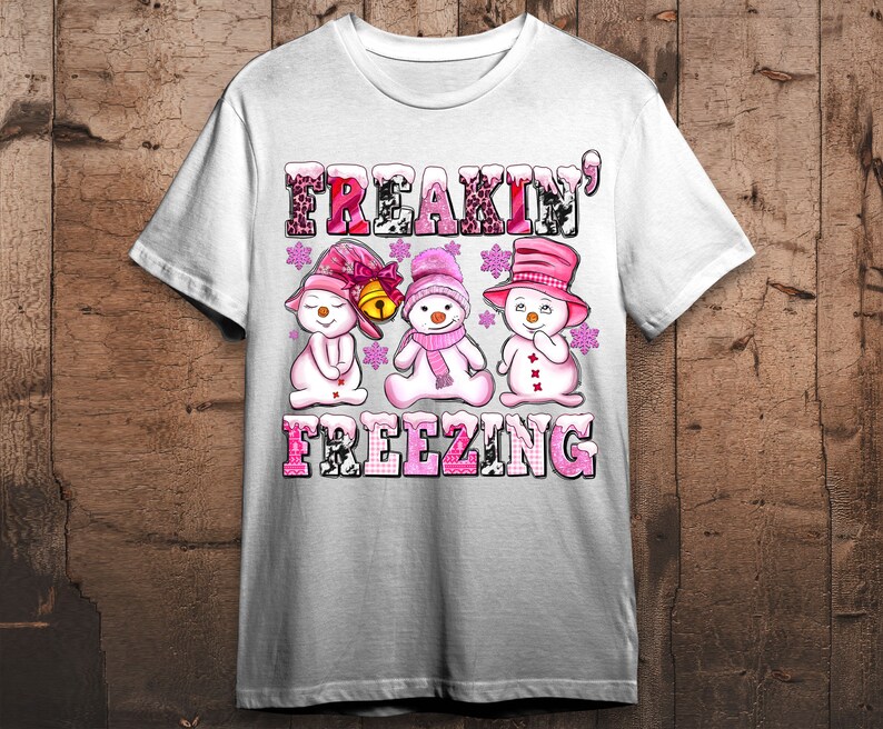 May include: White t-shirt with a pink and white graphic of three snowmen with the text "Freakin' Freezing" on it.