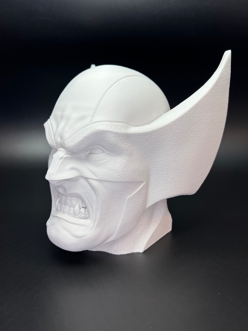 May include: A white bust of a character with a furrowed brow, bared teeth, and large, pointed ears. The sculpture has a textured surface and is set against a dark background. The character's expression is one of anger or aggression.