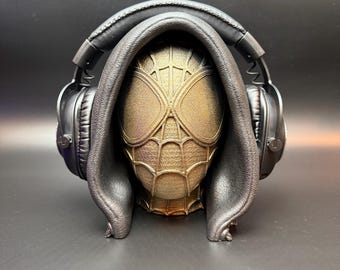 May include: A black headphone stand featuring a hooded figure in the shape of a spider-man head. The stand is made from a soft, black material and has a smooth, matte finish.