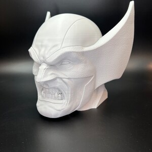 May include: A white 3D-printed bust of Wolverine, featuring his iconic mask with pointed ears and a snarling expression. The sculpture showcases detailed textures and sharp lines, capturing the character's fierce demeanor. The bust is a collectible item.
