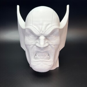 May include: A white, 3D-printed bust of a character's head, featuring a stern expression with furrowed brows and bared teeth. The head has pointed ear-like protrusions on each side.