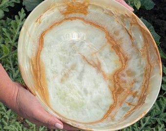 May include: A large, round bowl made of green and brown onyx. The bowl has a smooth, polished surface and is perfect for serving snacks or salads.