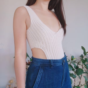 May include: A white knitted bodysuit with a plunging neckline and a high leg cut. The bodysuit is made of a soft, stretchy fabric and has a ribbed texture.