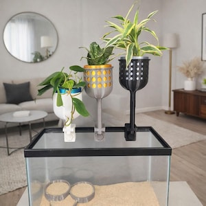 May include: Three decorative plant holders in white, silver, and black, each with a unique design. The holders are attached to a glass aquarium, with plants in each. The holders are designed to hold small plants.