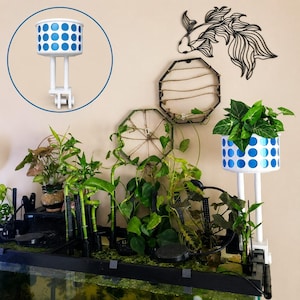 May include: A white cylindrical plant holder with a blue polka dot pattern, mounted on two vertical white poles with a clamp base. The holder is positioned on the right side of a fish tank filled with various green aquatic plants and decor.