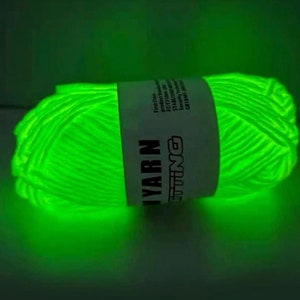 Può includere: Un gomitolo di filato verde brillante che brilla al buio. Il filato è avvolto attorno a un'etichetta bianca su cui è scritto "Yarn Knitting".