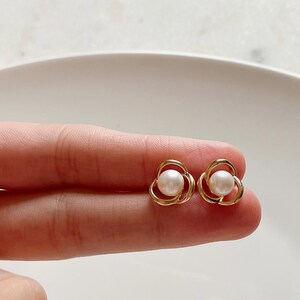 May include: A pair of gold flower-shaped earrings with a single pearl in the centre of each flower.