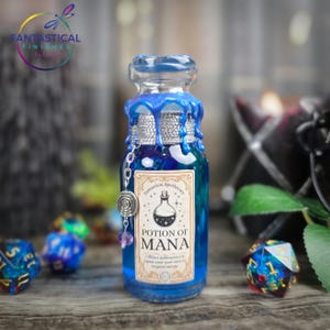 May include: A blue glass potion bottle with a silver chain and charm. The bottle has a label that reads "Potion of Mana". The bottle is decorated with blue wax and is surrounded by dice.