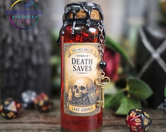 May include: A glass bottle labeled "Potion of Death Saves" with a skull graphic, designed for D&D dice rolling. The bottle has a cork top sealed with black wax and a decorative chain with a key charm. The potion is red, and the label reads "Last Chance".