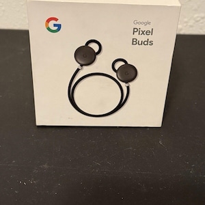 May include: A white box with the Google logo and the text "Google Pixel Buds" on it. The box shows a black pair of wireless earbuds with a black cord.
