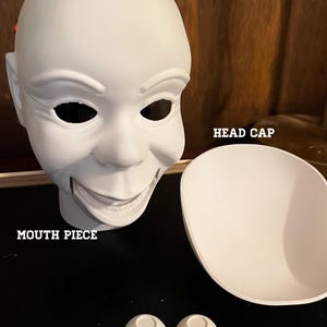 May include: A white doll head sculpt with a separate head cap, a mouth piece, and two spherical eyes. The components are labeled with the text HEAD SCULPT, HEAD CAP, MOUTH PIECE, and EYES. The doll head features a wide, smiling expression.