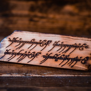 May include: A wooden sign with the inscription "One Ring to rule them all, One Ring to find them, One Ring to bring them all and in the darkness bind them" in Elvish script.