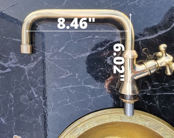 May include: Gold-toned faucet with a curved spout and a cross-shaped handle. The faucet is 8.46 inches wide and 6.02 inches tall.