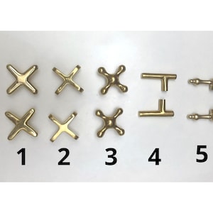May include: A collection of brass-colored hardware components, including cross-shaped handles, spherical knobs, and T-shaped and bar-shaped pieces. The items are numbered 1 through 5, and are likely for furniture or fixtures.
