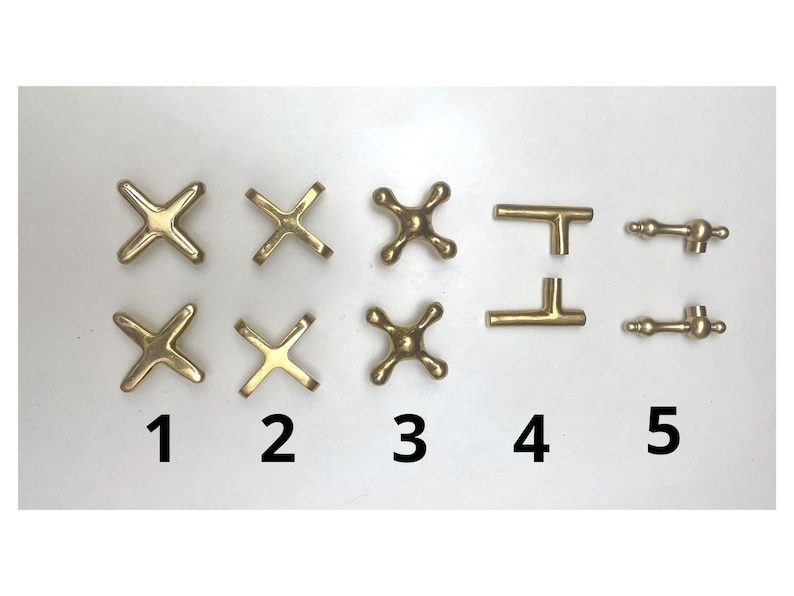 May include: A collection of brass-colored hardware components, including cross-shaped handles, spherical knobs, and T-shaped and bar-shaped pieces. The items are numbered 1 through 5, and are likely for furniture or fixtures.