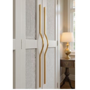 May include: Close-up of a white cabinet door with a woven mesh panel and two curved gold-colored handles. The cabinet is part of a larger piece of furniture, possibly a wardrobe or storage unit.