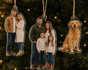 Può includere: Tre decorazioni natalizie in acrilico trasparente con stampe fotografiche personalizzate. Un ornamento mostra una coppia, un altro una famiglia di quattro persone e il terzo un golden retriever. Ogni pezzo pende da un cordino dorato.