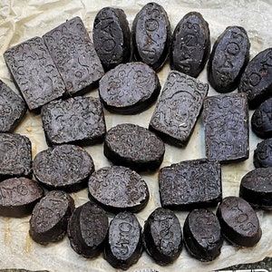 Può includere: Una collezione di 20 saponette marroni scure con vari disegni in rilievo, tra cui motivi floreali e la parola "SOAP". Le saponette sono disposte su un pezzo di carta da forno.