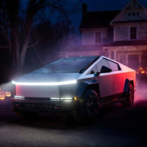 K&ouml;nnte beinhalten: Ein silberner, kantiger Elektro-Pickup mit einer markanten horizontalen LED-Lichtleiste an der Front, dunklen R&auml;dern und scharfen geometrischen Karosserieteilen, der nachts in einer Einfahrt mit leuchtenden K&uuml;rbissen im Hintergrund steht.