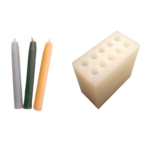 May include: Three slender taper candles in gray, green, and orange, next to a cream-colored candle holder with multiple holes. The candles have a smooth finish and are unlit.