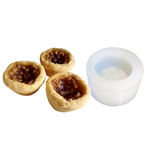 Puede incluir: Tres pequeñas tartaletas doradas, rellenas de una sustancia marrón y pegajosa y cubiertas con nueces picadas, con un molde de silicona blanco.