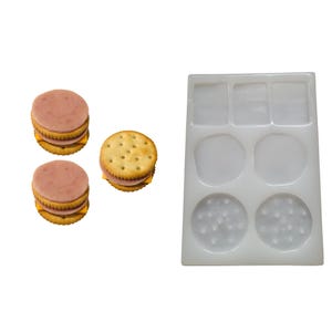 May include: An image shows three miniature cracker sandwiches with ham and cheese, alongside a clear silicone mold with various shaped cavities. The mold includes square, round, and cracker-shaped spaces, likely for crafting.