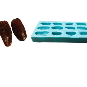 Pode incluir: Uma forma de silicone azul com 12 cavidades em forma de tâmaras. Duas tâmaras são mostradas ao lado da forma.