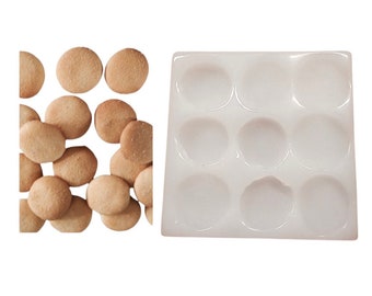 May include: A white silicone mould with nine round cavities for making cookies or other treats. A pile of small, round, light brown cookies are shown next to the mould.