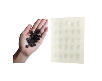 May include: A white silicone mold with 24 individual cavities shaped like coffee beans. The mold is designed for making chocolate or other edible treats.