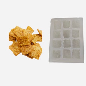 Könnte beinhalten: Eine weiße Silikonform mit 12 quadratischen Fächern, perfekt zum Herstellen von Eiswürfeln oder anderen kleinen Leckereien. Außerdem ist ein Haufen knuspriger, goldbrauner Cerealienquadrate zu sehen.