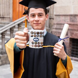 May include: A person in a graduation gown and cap holds a white mug featuring portraits of U.S. presidents and the White House logo. The person also holds a rolled diploma tied with a blue ribbon. The gown has gold accents.