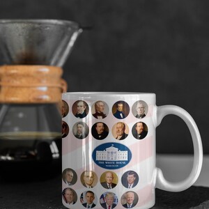 May include: White ceramic mug featuring portraits of U.S. presidents in circular frames. The mug has a design of pink and white stripes and a blue oval with the White House and the text "THE WHITE HOUSE WASHINGTON".