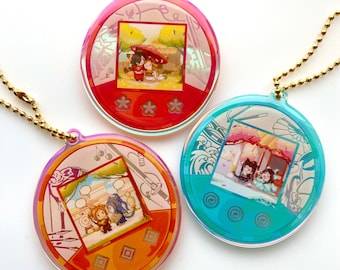 Op de afbeelding: Drie kleurrijke, ronde acryl bedels met gouden kettingbevestigingen. Elke bedel heeft een andere illustratie in een vierkant frame, tegen een achtergrond van rood, oranje en blauw. De bedels hebben een retro, digitaal huisdierontwerp.