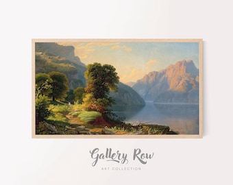 May include: A framed landscape painting depicting a serene lake surrounded by towering mountains under a soft golden sky. The foreground features a lush green path lined with trees and rocks, leading toward the calm water reflecting the light.