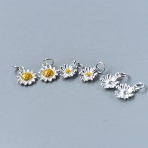 May include: Six silver daisy charms with yellow centers. The charms are perfect for adding a touch of whimsy to jewelry projects.
