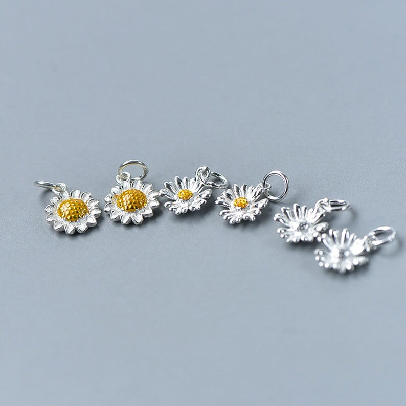 May include: Six silver daisy charms with yellow centers. The charms are perfect for adding a touch of whimsy to jewelry projects.