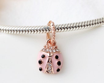 May include: A rose gold ladybug charm with a pink body and black spots. The charm is embellished with clear crystals and hangs from a rose gold bail. The charm is shown on a silver chain.