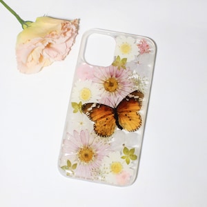 May include: Clear phone case with a butterfly and flowers. The case features a vibrant orange and brown butterfly, surrounded by pink and white flowers. The case is designed to fit a smartphone.