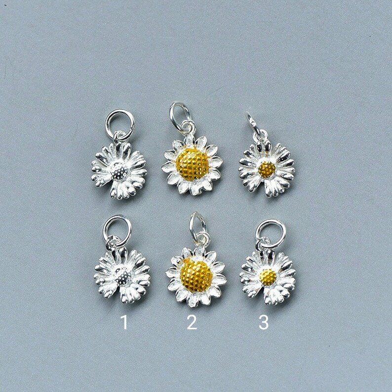 May include: Six silver daisy charms with yellow centers. Three charms have a solid yellow center and three charms have a silver center with a yellow center.