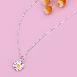 May include: A delicate silver chain necklace with a small white daisy pendant featuring a yellow center.